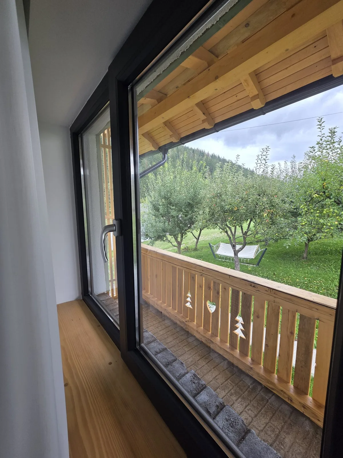 Ușa spre balconul de lemn, cu livada și dealurile în față