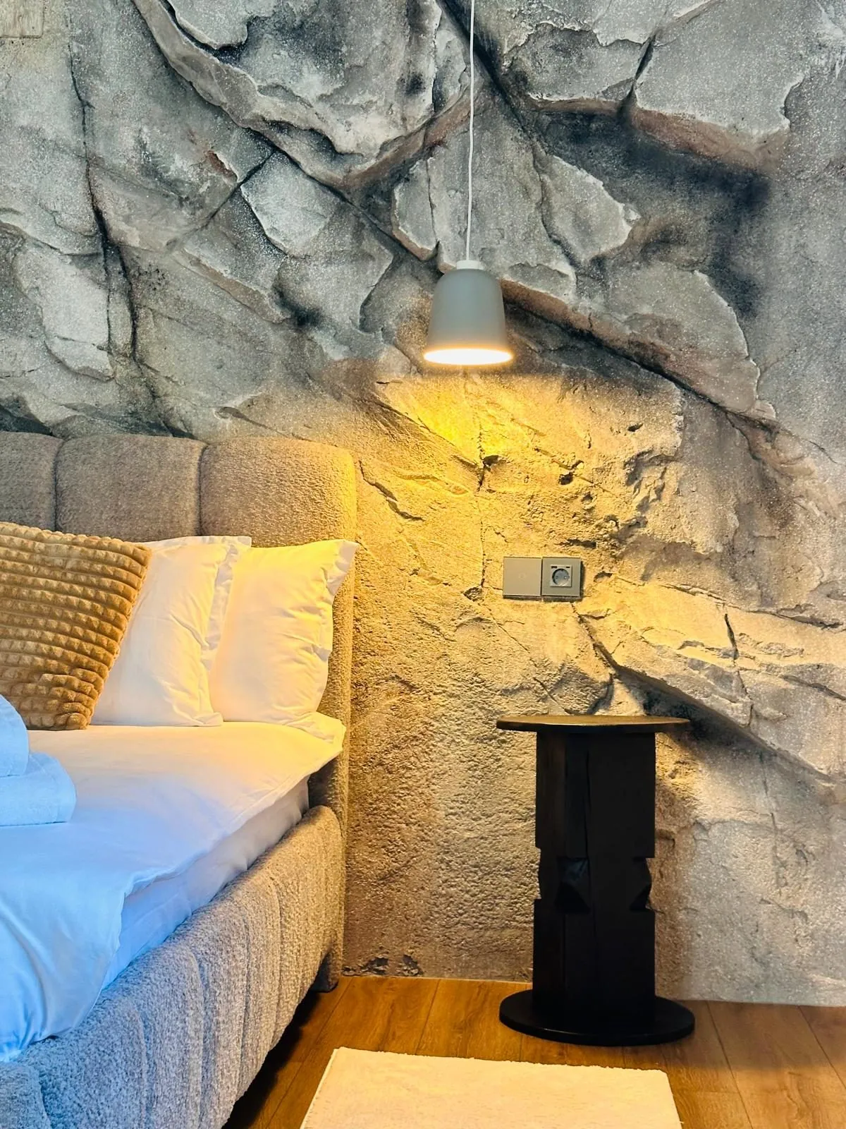 Noptiera din lemn sculptat lângă pat, sub lampa din rocă