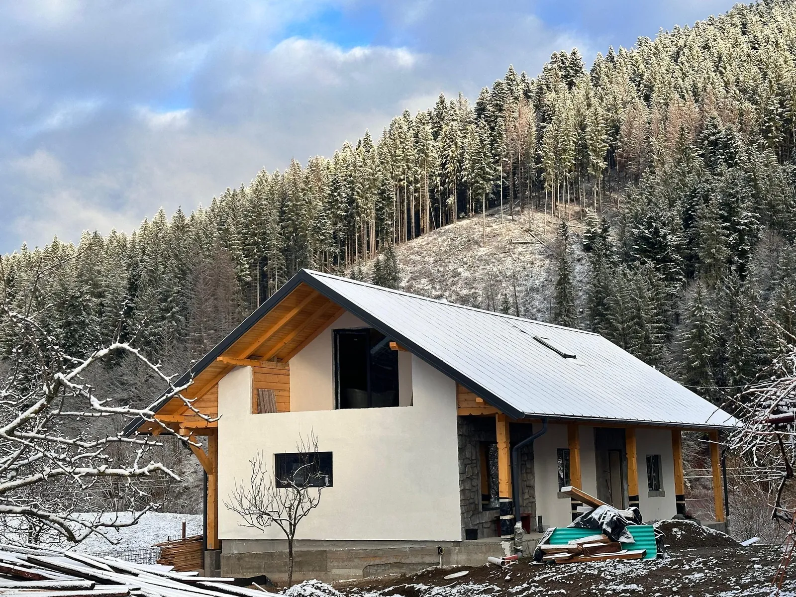 Casa în lucru, iarna, cu pădurea acoperită de zăpadă în spate