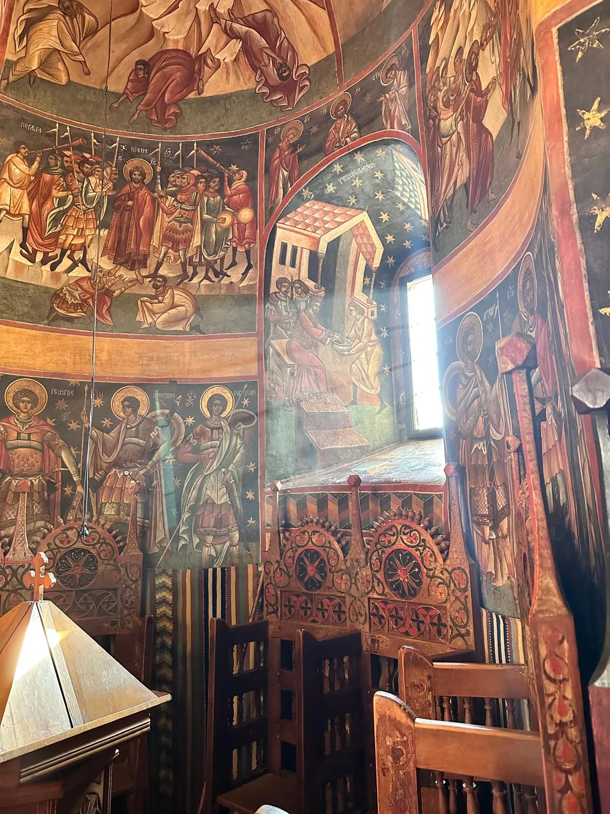 Interiorul bisericii Voroneț, cu fresce în tonuri calde și strane de lemn