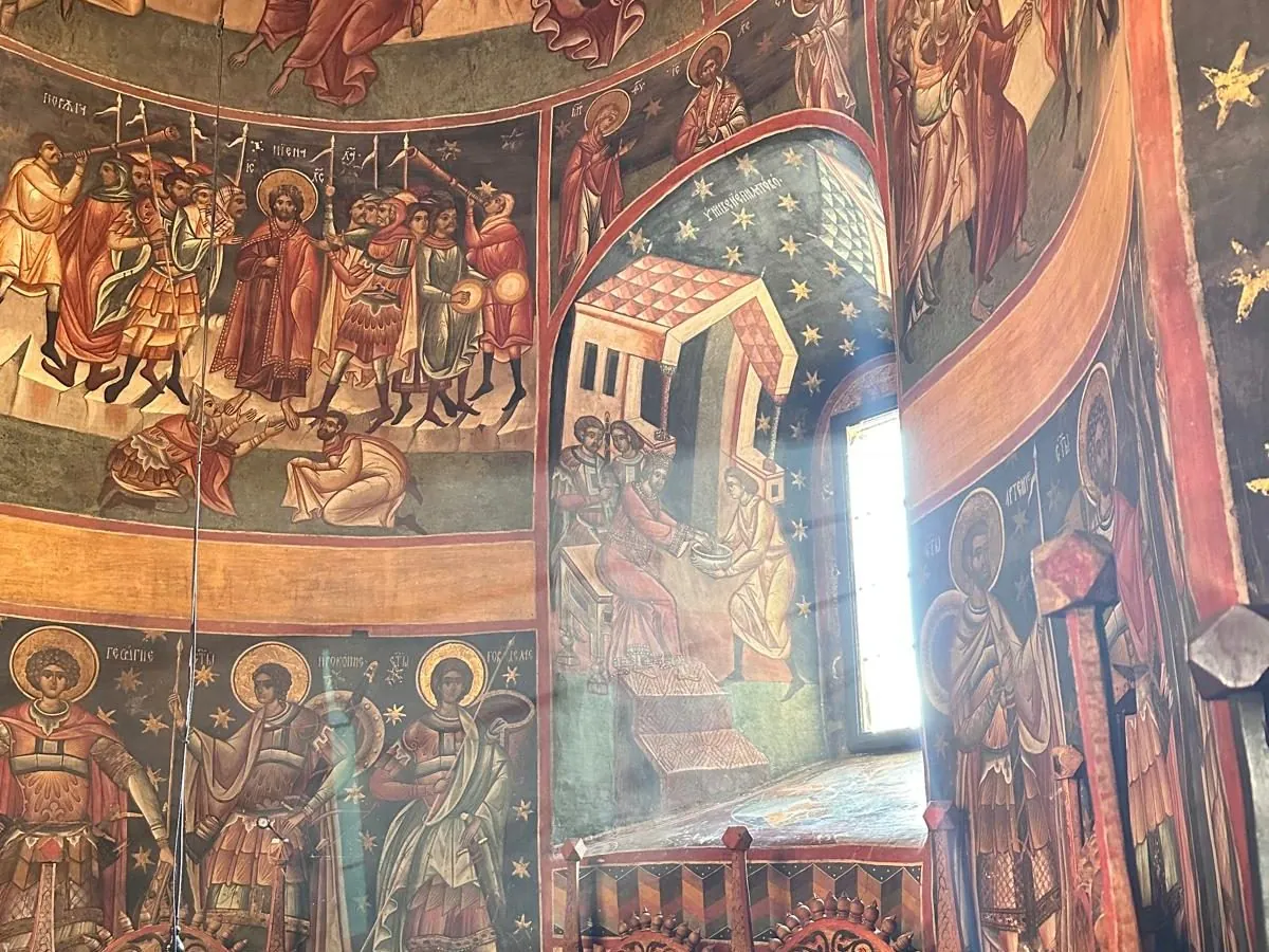 Fresce în interiorul bisericii Voroneț, cu sfinți și scene biblice în tonuri calde, lângă o fereastră